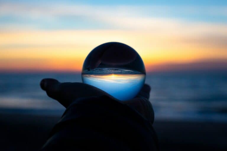 Betrachtung eines Sonnenaufgangs durch eine Glaskugel in der Hand eines Menschen