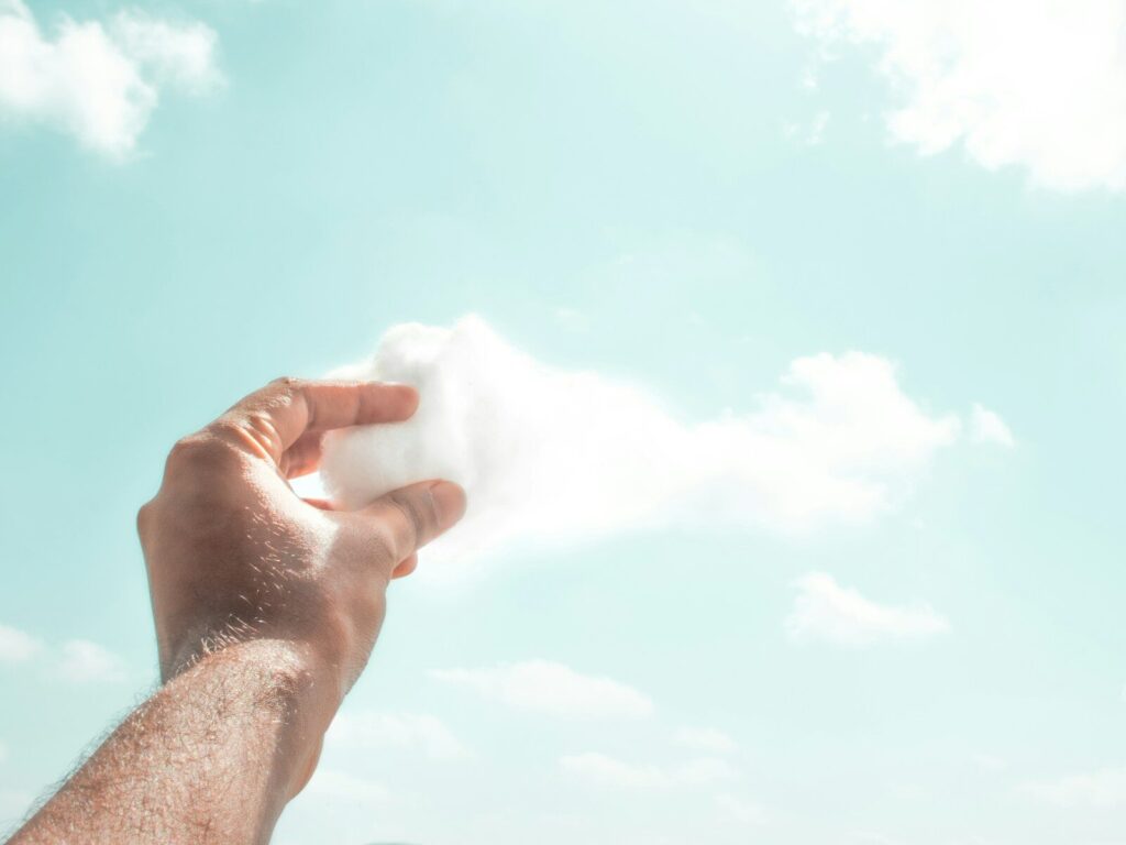 eine Hand hält einen Wattebausch vor eine Wolke